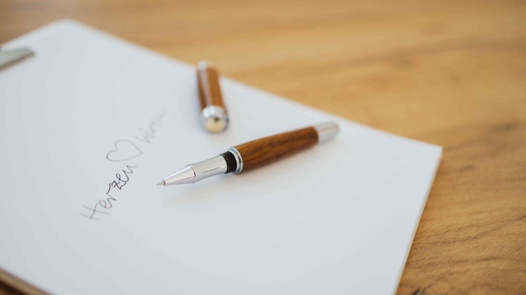 Auf dem Bild ist ein Blatt Papier mit der Aufschrift Herzenhören zu sehen. Auf dem Papier liegt ein Stift.